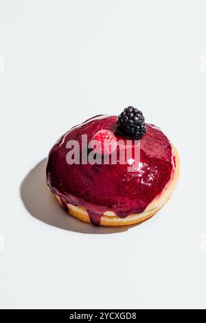 Una ciambella ripiena di cheesecake ricoperta da una glassa di frutti di bosco e decorata con lampone e mora freschi, questo ricco e fruttato dessert è cremoso Foto Stock