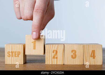 Uomo che mette un cubo di legno con il numero 1 tra gli altri con la parola Step e il numero 2 sul tavolo, primo piano. Concetto passo-passo Foto Stock