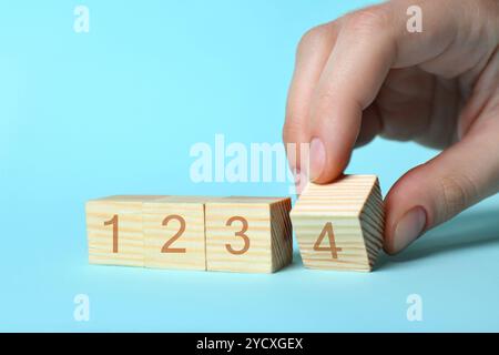 Uomo che mette un cubo di legno con la cifra 4 a fila di altri numeri su sfondo azzurro, primo piano. Concetto passo-passo Foto Stock