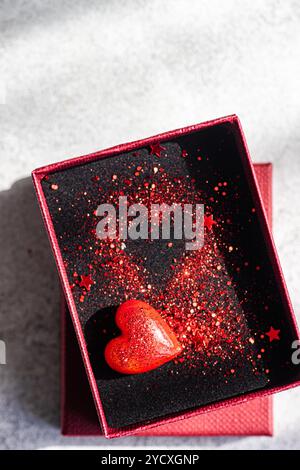 Un vivace oggetto rosso a forma di cuore poggia all'interno di una scatola, splendidamente decorata con brillantini rossi che riflettono un tema romantico Foto Stock