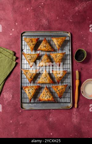 Samosas al forno ripieni di tofu cosparse di semi di sesamo catturati su un vivace sfondo rosso per una presentazione culinaria colorata Foto Stock