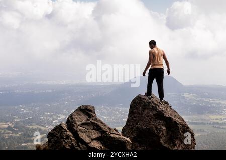 Un uomo solitario si erge su un affioramento roccioso, affacciato sulla distesa del Parco Ajusco di città del Messico. La sua postura riflette un momento di trionfo e contemplazione Foto Stock