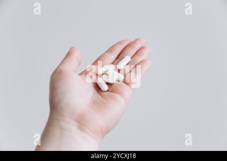 Un'immagine ravvicinata che mostra una mano aperta che tiene diverse pillole bianche allungate lo sfondo è in grigio chiaro uniforme, sottolineando la semplicità e il fascino Foto Stock