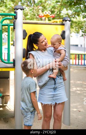 Una madre gioiosa trascorre del tempo di qualità con il figlio e il bambino in un parco giochi, coinvolgendo giocosamente e condividendo un umore allegro in un parco pubblico Foto Stock