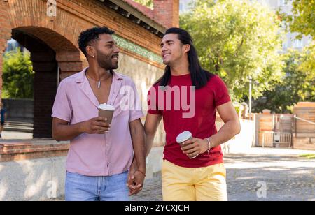 Una allegra coppia gay gode di una piacevole passeggiata attraverso un paesaggio urbano, condividendo un momento di luce e un caffè, incarnando la diversità e gli inclusivi Foto Stock