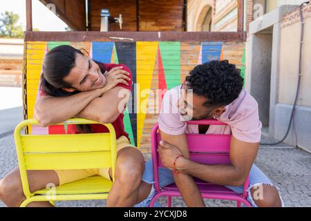 Un momento di gioia tra una coppia gay mentre abbracciano sedie con uno sfondo colorato, l'immagine cattura il calore e l'intimità dei loro colleghi Foto Stock