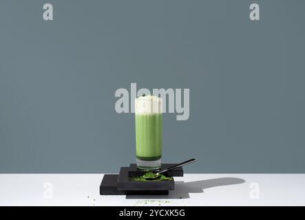 Un allettante bicchiere di tè matcha freddo sormontato da uno strato di panna montata, presentato su uno sfondo minimalista con polvere di matcha sparsa. Foto Stock
