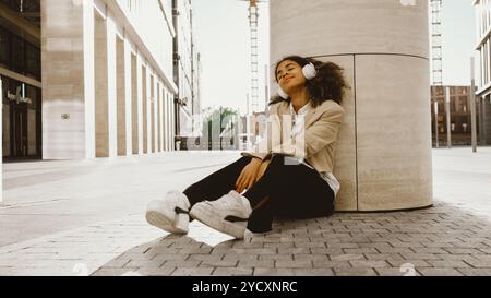 La giovane donna d'affari sta godendo un momento di pace mentre ascolta la musica con le sue cuffie, trovando tranquillità nel vivace ambiente urbano Foto Stock