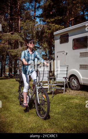 Donna sulla bicicletta elettrica in appoggio al campeggio. Vacanza per la famiglia in viaggio, viaggio vacanza in camper, caravan VR auto vacanza. Foto Stock