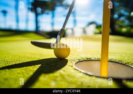 Mini Golf sfera gialla con un bat in prossimità del foro al tramonto Foto Stock