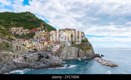 Passeggia per le vivaci strade di Manarola mentre il sole attraversa le nuvole, illuminando le case colorate arroccate sulle scogliere, affacciate sul tranquillo mare delle pittoresche cinque Terre. Foto Stock