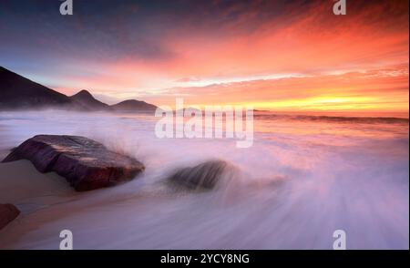 Il sole dell'oceano sorge mentre le grandi onde si infrangono sulla spiaggia Foto Stock