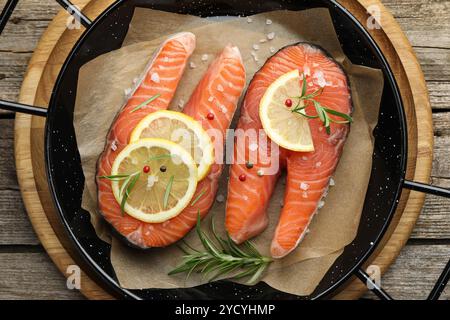 Bistecche di salmone crude fresche con spezie in padella su un tavolo di legno, vista dall'alto Foto Stock