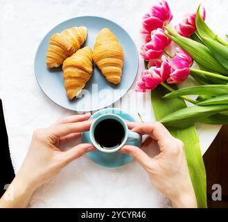 Ragazza con croissant e caffè, un bouquet di tulipani rosa, mattina felice. Foto Stock