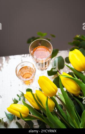 Tulipani gialli su un tavolo bianco con un bicchiere di vino rosa, primo piano Foto Stock