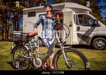 Donna sulla bicicletta elettrica in appoggio al campeggio. Vacanza per la famiglia in viaggio, viaggio vacanza in camper, caravan VR auto vacanza. Foto Stock