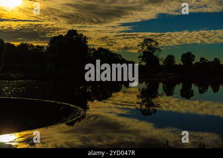 Un paesaggio di tranquillità: Il cielo notturno sul fiume. La luce della luna piena brilla attraverso le nuvole e si riflette nell'acqua ferma Foto Stock