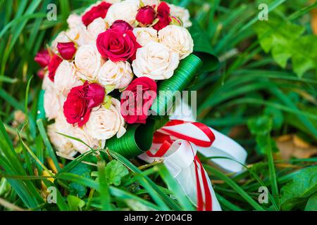 Bouquet nuziale di rose rosse e bianche adagiate sull'erba Foto Stock