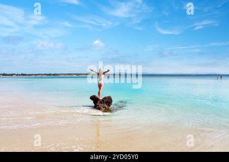 Donna in costume da bagno bianco, in piedi su una roccia circondata dalle splendide acque incontaminate di Jervis Bay Australia. Spazio per la copia Foto Stock