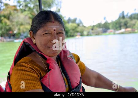 Una radiosa donna dell'India del Sud con un giubbotto di salvataggio sorride brillantemente durante un giro in barca soleggiato su un lago tranquillo. Foto Stock