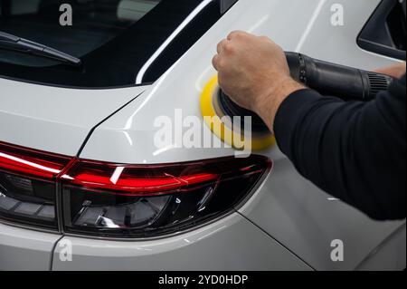 Processo di lucidatura della superficie bianca della carrozzeria della vettura con una lucidatrice orbitale. Foto Stock