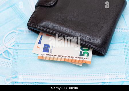 Nero uomo portafoglio con euro soldi dentro sul blu monouso maschere mediche viso. Permuta maschere mediche. Affari durante una pandemia o un'epidemia Foto Stock