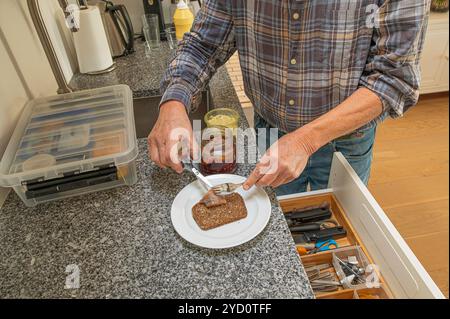 Un uomo è in piedi in cucina a preparare un panino con aringhe su un pane di segale, Danimarca, 24 ottobre 2024 Foto Stock