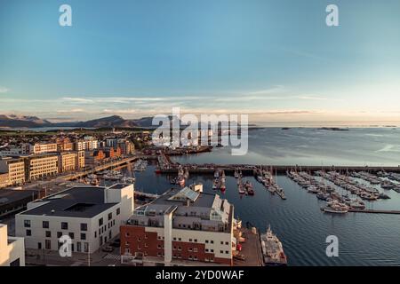 Il vivace porto di Bodo si anima al crepuscolo, con barche colorate ancorate vicino a edifici incantevoli sullo splendido sfondo costiero di Nordlan Foto Stock