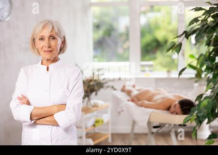 Massaggiatrice professionale per anziani sicura di sé in piedi nella sala massaggi Foto Stock