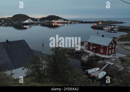 Mentre la notte si avvicina alle isole Lofoten, una tranquilla baia riflette l'ultima luce del crepuscolo, evidenziando edifici pittoreschi e acque tranquille circondate Foto Stock