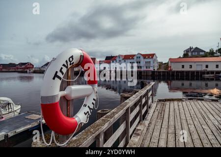 Un salvagente si erge in modo prominente sul molo di legno di Henningsvær, incorniciato da edifici colorati e acque calme. Le isole Lofoten creano un pittoresco paesaggio Foto Stock