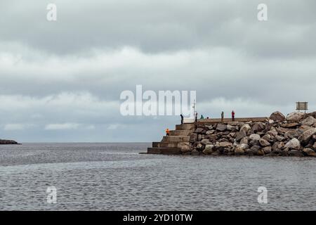 Questo paesaggio costiero ospita appassionati di pesca in un promontorio roccioso nelle isole Lofoten, circondato da acque calme e formazioni nuvolose uniche Foto Stock