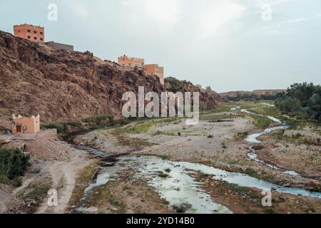 Annidato in Marocco, questa posizione presenta una splendida valle con un torrente serpeggiante delimitato da scarpate rocciose, che mostra antiche strutture e. Foto Stock
