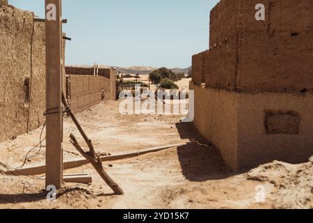 Questo luogo espone antichi edifici pueblo nel deserto del Sahara, con suolo secco e paesaggi sabbiosi sotto un cielo azzurro e limpido, mettendo in risalto il suo Foto Stock