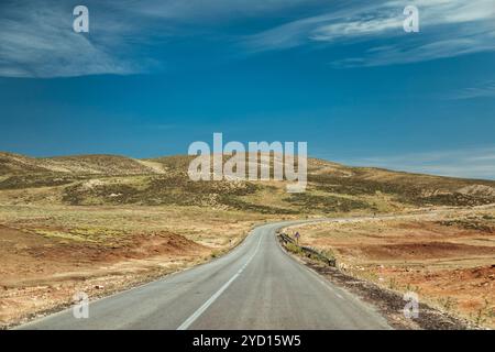 Una tortuosa strada sterrata si estende attraverso i calanchi del Marocco, circondati da un vasto paesaggio di colline e praterie sotto un cielo blu brillante. Il terr Foto Stock