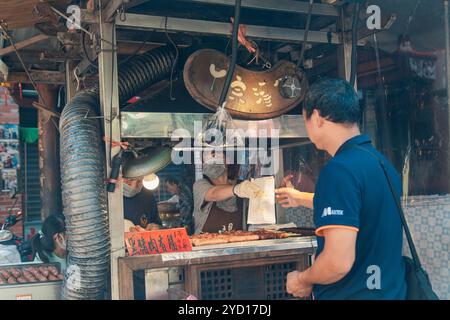 Taipei, Taiwan - 10 ottobre 2019: Trafficato venditore ambulante che serve deliziosi spuntini ad un cliente nel vivace mercato alimentare di Taipei Foto Stock