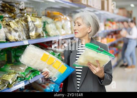 Signora anziana interessata che legge etichetta su confezioni di noodles asiatici nel supermercato Foto Stock