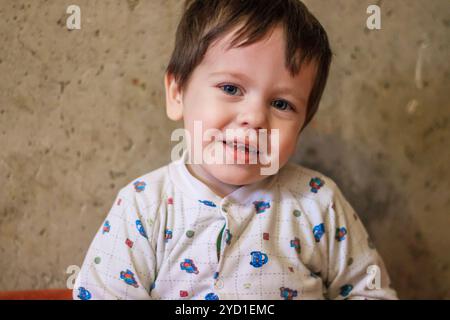 Ritratto di un ragazzo sullo sfondo di un muro di cemento. Il ragazzo sorride. Il ragazzo sta guardando la telecamera. Foto Stock