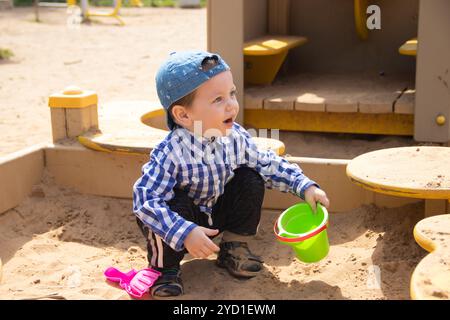 Il ragazzo gioca nella sabbia nella scatola di sabbia. Giochi per bambini. Sandbox. Scatole di sabbia per bambini. Felice ragazzo. Foto Stock