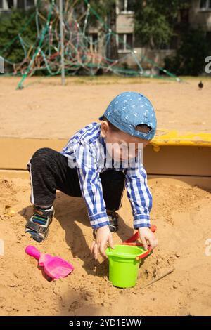 Il ragazzo gioca nella sabbia nella scatola di sabbia. Giochi per bambini. Sandbox. Scatole di sabbia per bambini. Felice ragazzo. Foto Stock