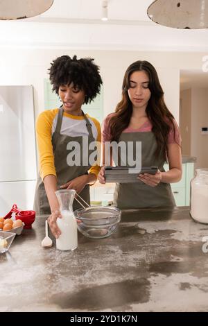Natale, amici che cucinano insieme in cucina, usando un tablet per consigli sulle ricette, a casa Foto Stock