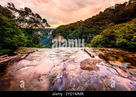 Vedute panoramiche della valle attraverso il flusso d'acqua poco profondo che si riversa sulla scogliera delle Blue Mountains. Con cielo al tramonto e luce soffusa e rif Foto Stock