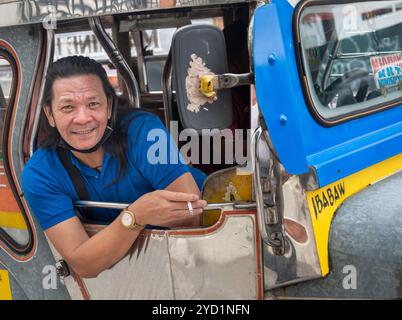 Manila-13 gennaio 2023: Ritratto di un simpatico autista di jeepney filippino, che si appoggia fuori dalla finestra e sorride, che tiene in mano una mezza sigaretta affumicata, durante il Foto Stock