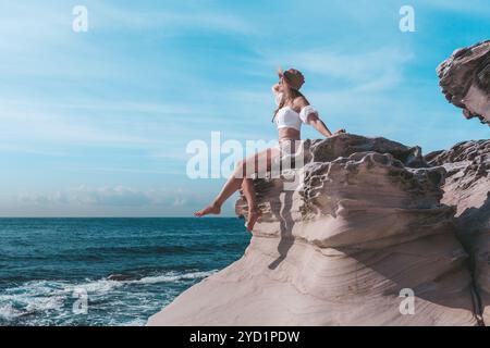 Donna che si gode il sole estivo, seduta accanto all'oceano e indossa un cappello Foto Stock