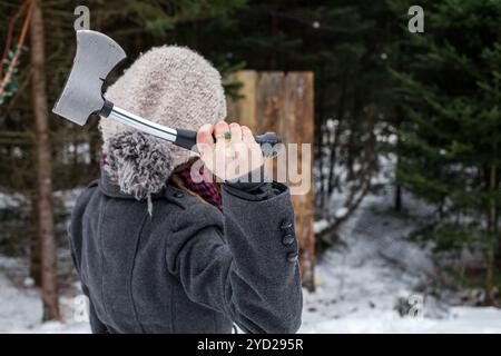 Ragazza vestita in abbigliamento invernale detiene un'ascia di fronte a una tavola di legno come parte di un'ascia gettando la concorrenza Foto Stock