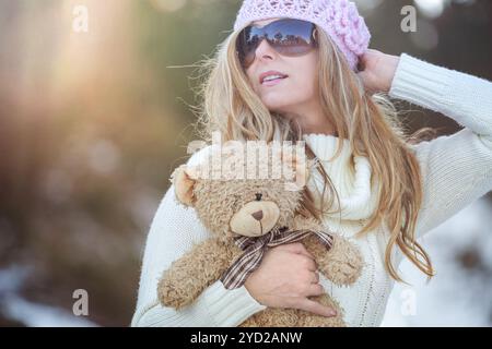 Donna che indossa un maglione in maglia spessa all'aperto sulla neve in inverno. Sta tenendo in mano un orso ripieno marrone generiale Foto Stock