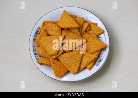 Croccanti e deliziose tortilla patatine triangolari su un piatto bianco al gusto di nachos messicano, poste su una superficie di legno chiaro. Foto Stock