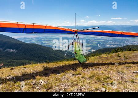 Deltaplano pilota in corsa e decollo. Vista panoramica sulle montagne della valle di Kootenay. Vista da dietro a volo Hang alider Foto Stock