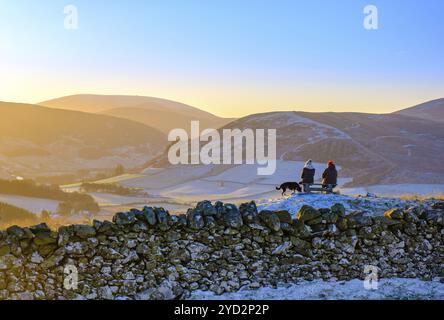 Due amici seduti su una panchina nella splendida campagna scozzese dopo Un'escursione in mattinata di gelata, con il loro cane Foto Stock