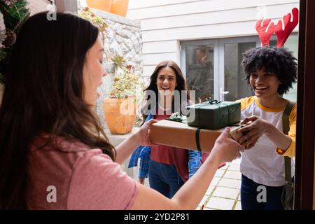 Amici femminili multirazziali che scambiano regali di natale a due passi, a casa Foto Stock